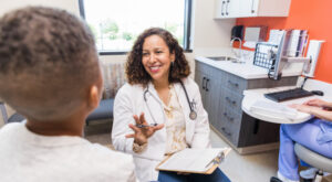 Mid adult female pediatrician smiles while talking with child